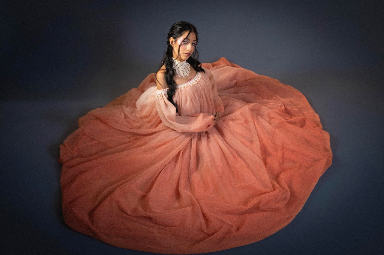 Diseño de Anna Rettally: vestido coral de gran volumen sobre fondo azul.